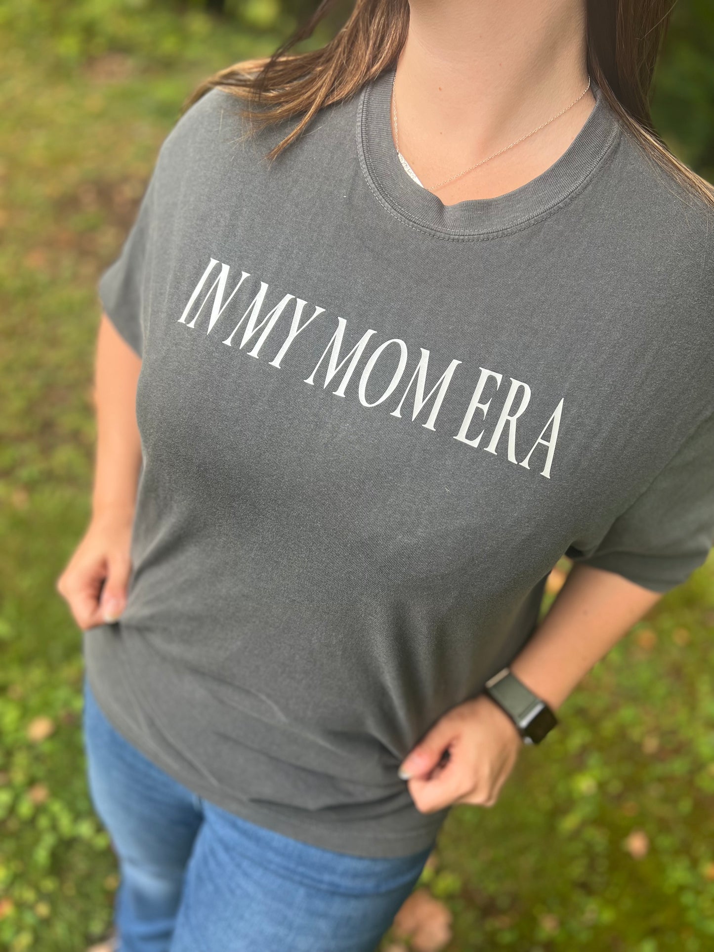 Close up of a mid-size woman wearing a charcoal graphic tee that says, "In My Mom Era."