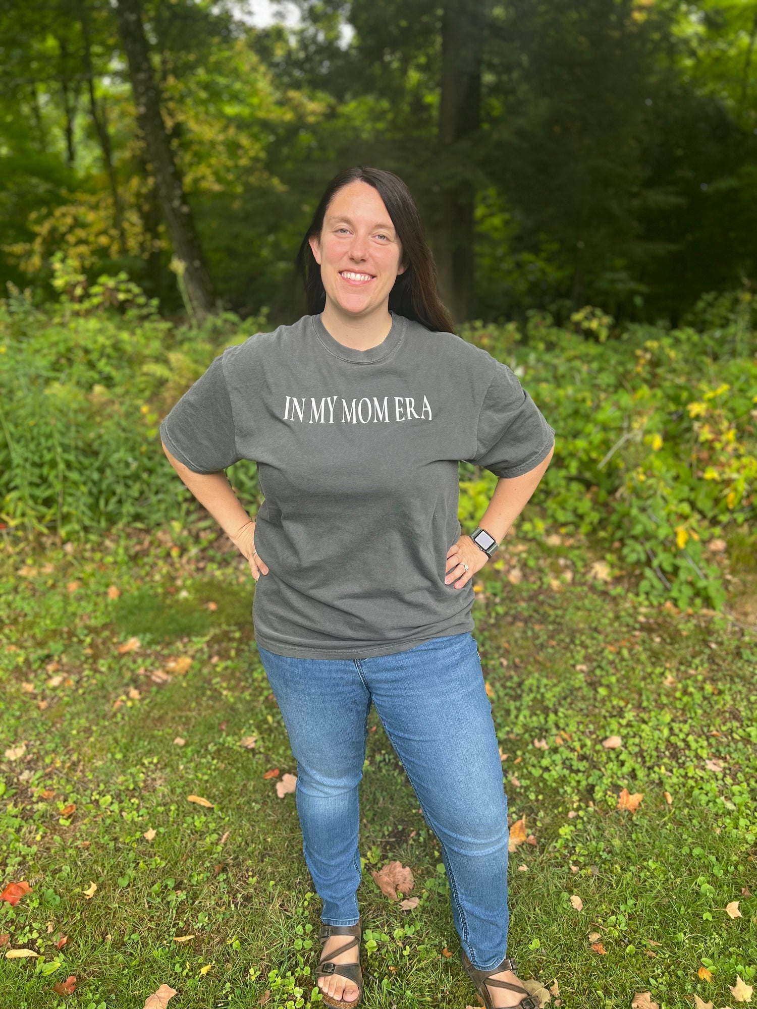 Mid-size woman in her thirties modeling a charcoal graphic T-shirt that says, "In My Mom Era."