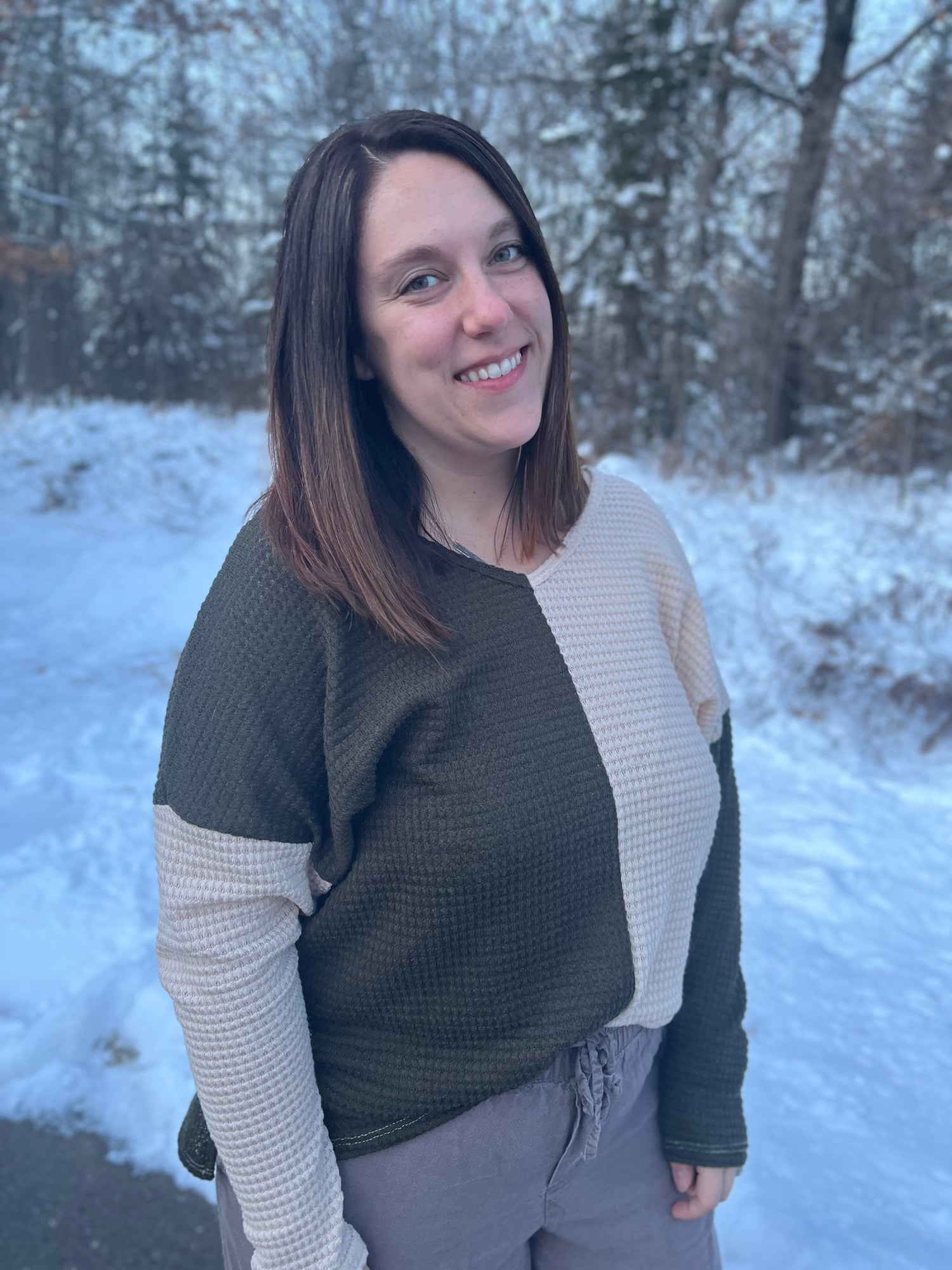 A woman in an olive green and beige white color-block long sleeve top. 