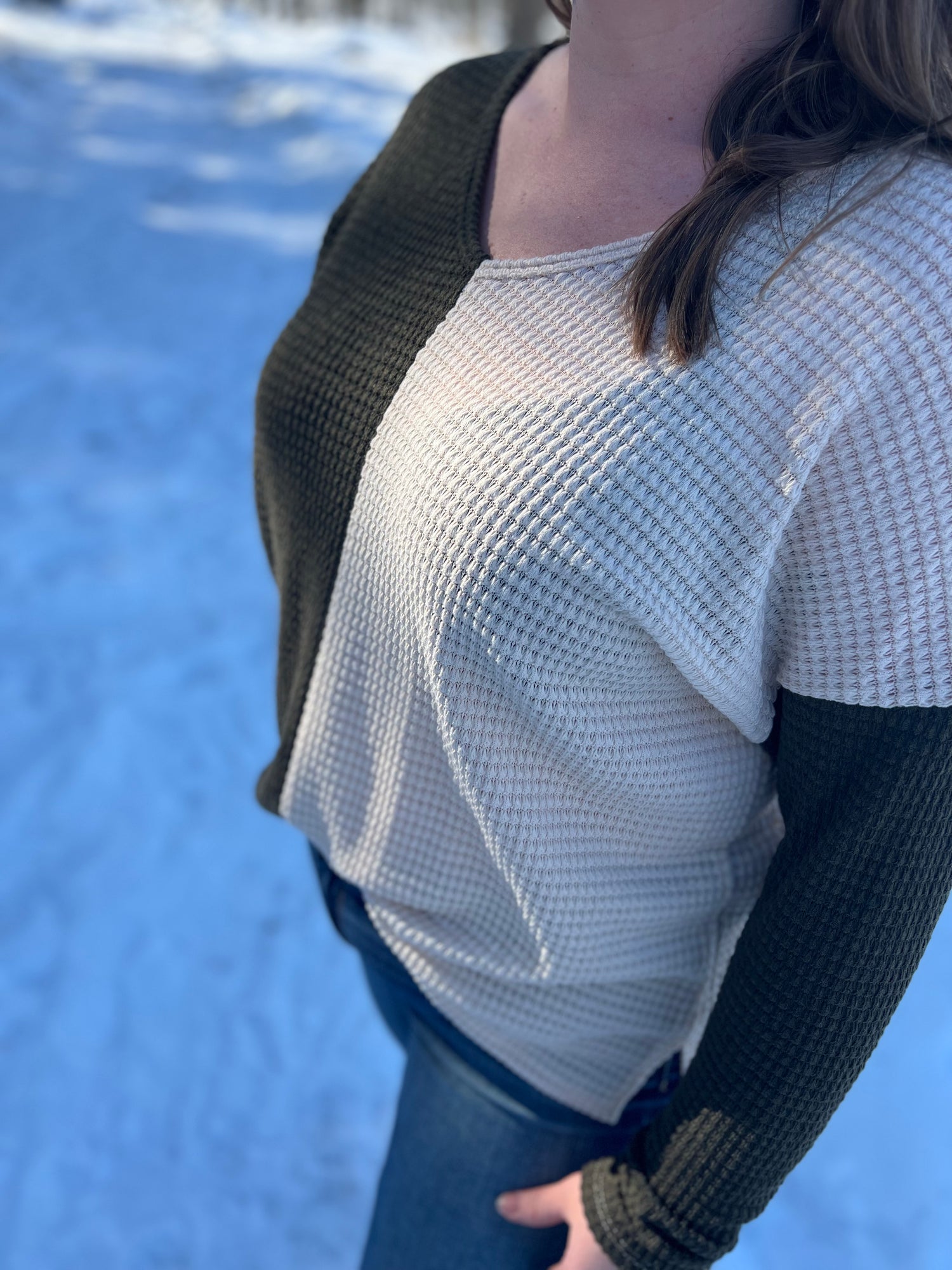 A woman in an olive green and beige white color-block long sleeve top. 