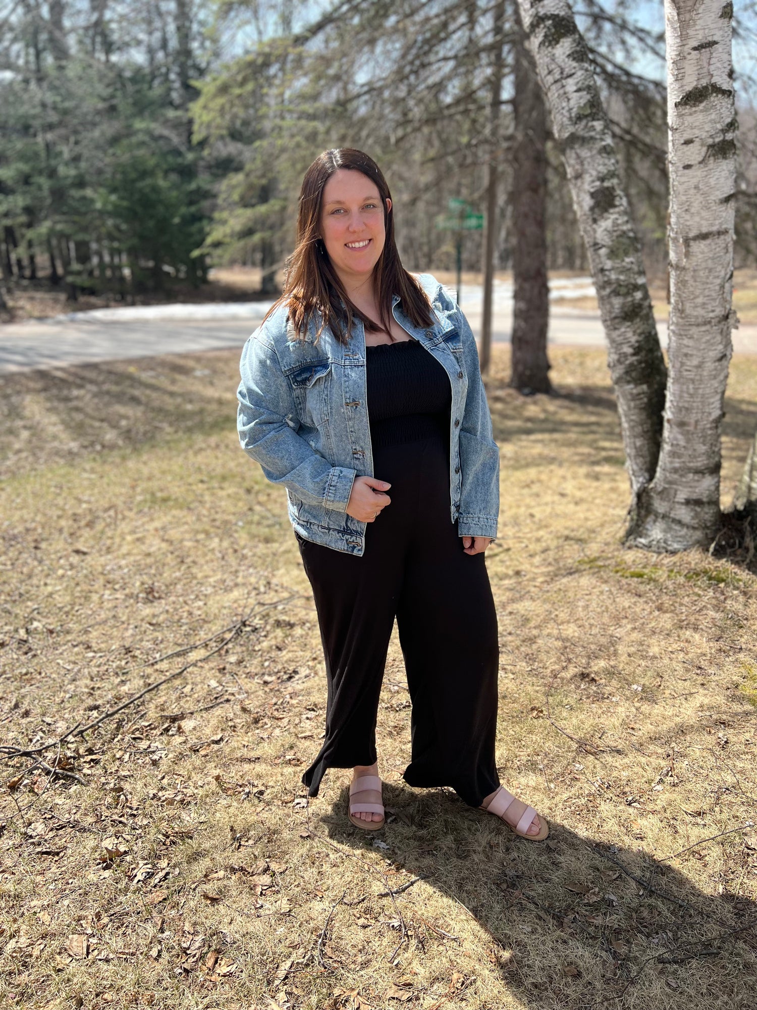 Black smocked jumpsuit with tied tank sleeves and long pants worn with our denim distressed jacket 